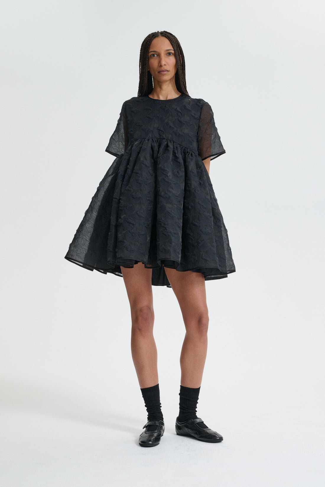 Black textured babydoll mini dress with short sleeves and a wide gathered skirt, worn with black socks and flat shoes
